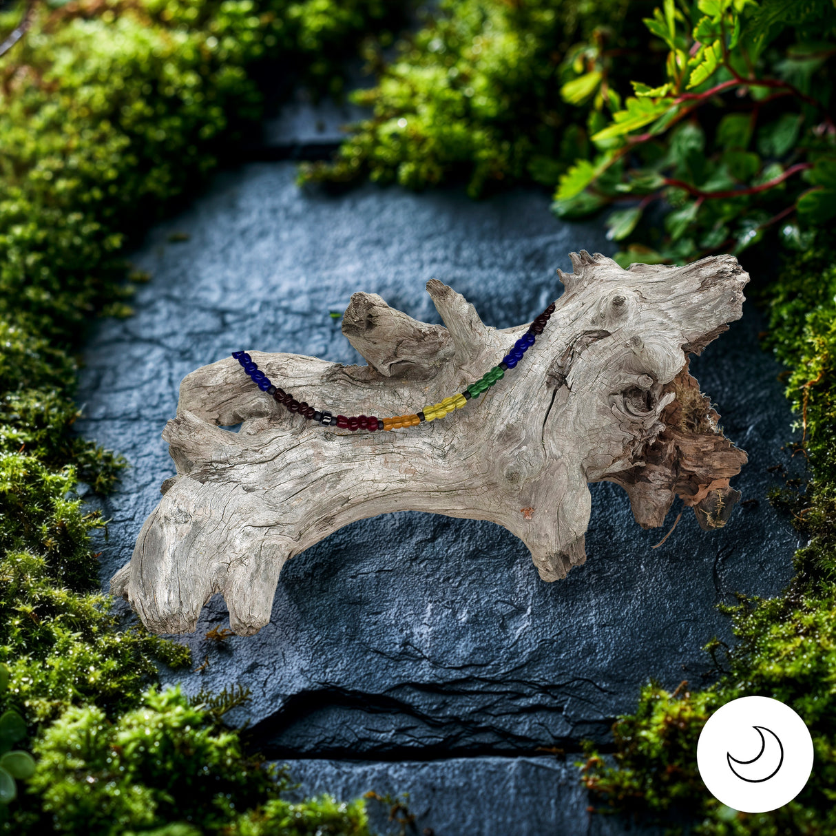 Pride rainbow bracelet on driftwood stand against stone surface surrounded by greenery
