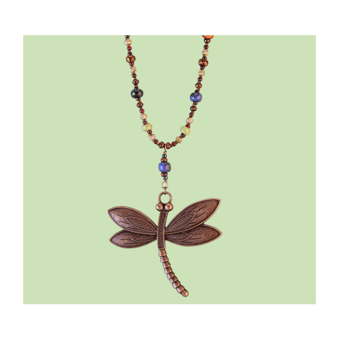 Close-up of an intricate 2.5-inch antiqued bronze dragonfly pendant showing detailed wing textures and earthy Picasso glass bead accents.
