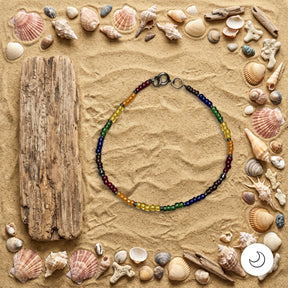 Pride rainbow beaded necklace on background of sand with seashells and driftwood