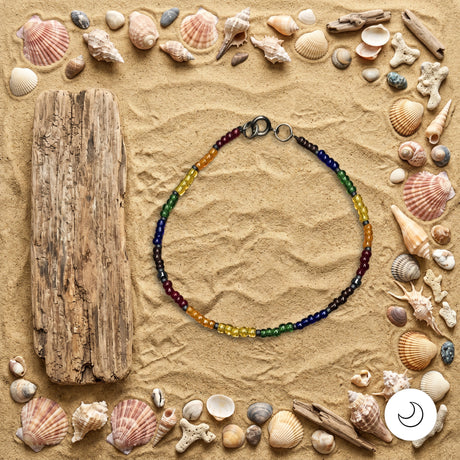Pride rainbow beaded necklace on background of sand with seashells and driftwood
