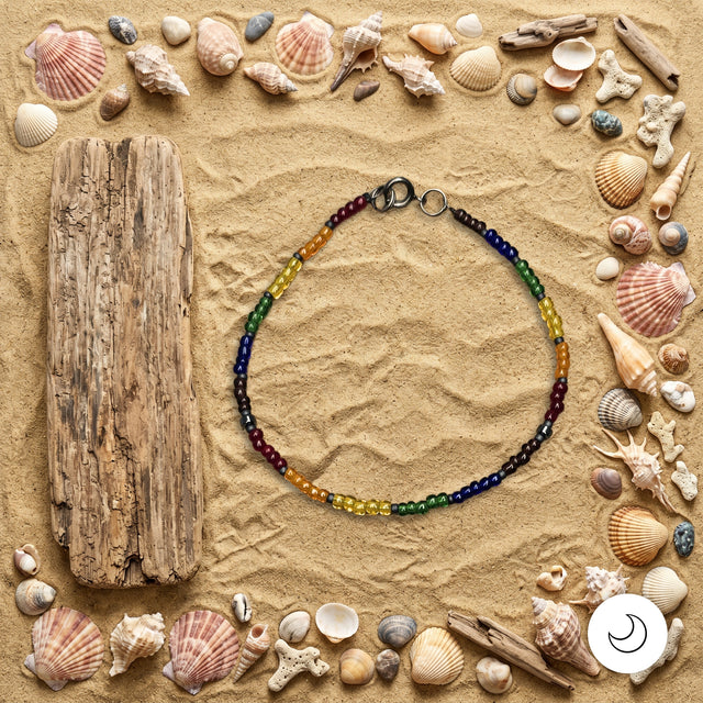 Pride rainbow beaded necklace on background of sand with seashells and driftwood