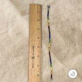 Colorful pride beaded bracelet next to a wooden ruler on a beige fabric background
