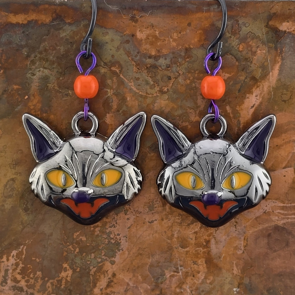 Black cat earrings with glowing yellow enamel eyes and hissing mouth shines with vibrant Halloween orange.