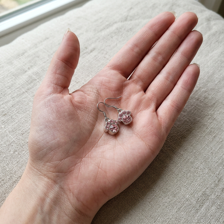 Pink paw print earrings resting in an open palm to show their petite 1/3 inch size
