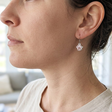 Pink crystal paw print earrings worn on an ear, showing the petite charm hanging just below the lobe
