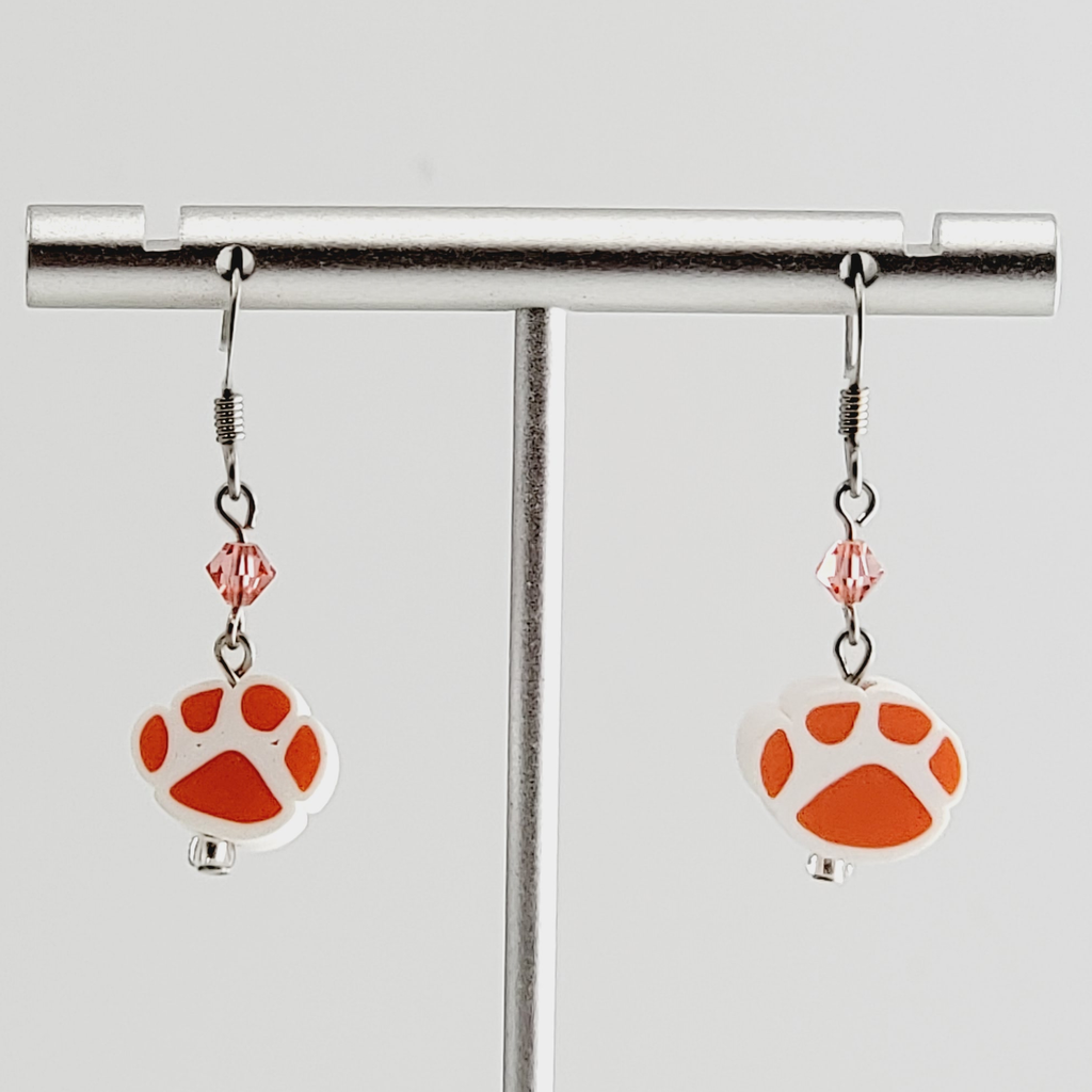 Handmade, hypoallergenic earrings with orange paw prints on white clay and accented with peach crystals