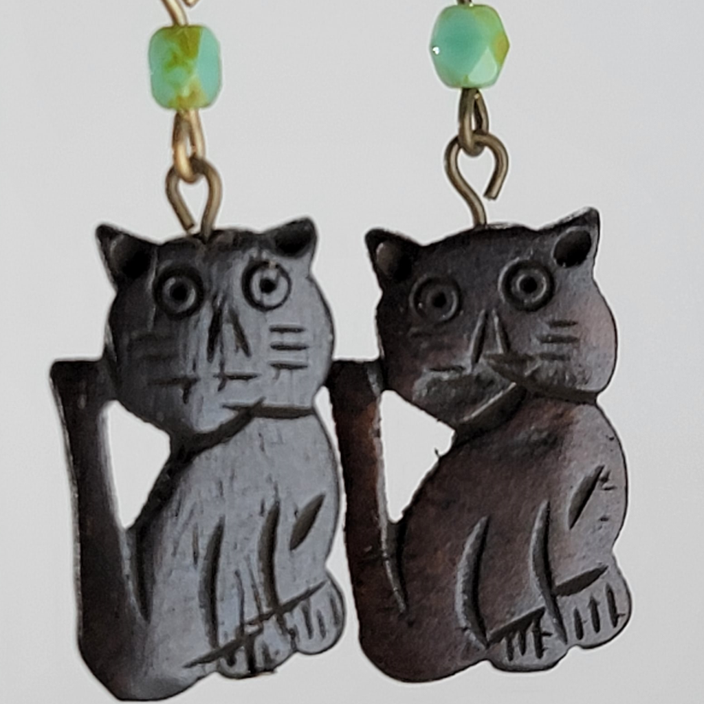 Earrings, brown cats with carved face and paw details. Above each cat is a small green bead. Ear wires are silver tone with a gold tone bead and spring.