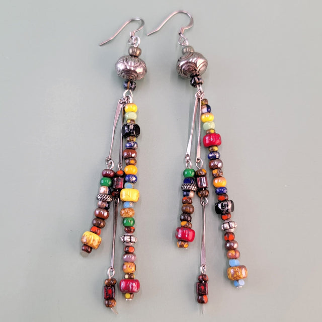 Long, dangly, colorful Boho earrings featuring three drops filled with richly-colored Picasso glass beads and silver-colored accents. 