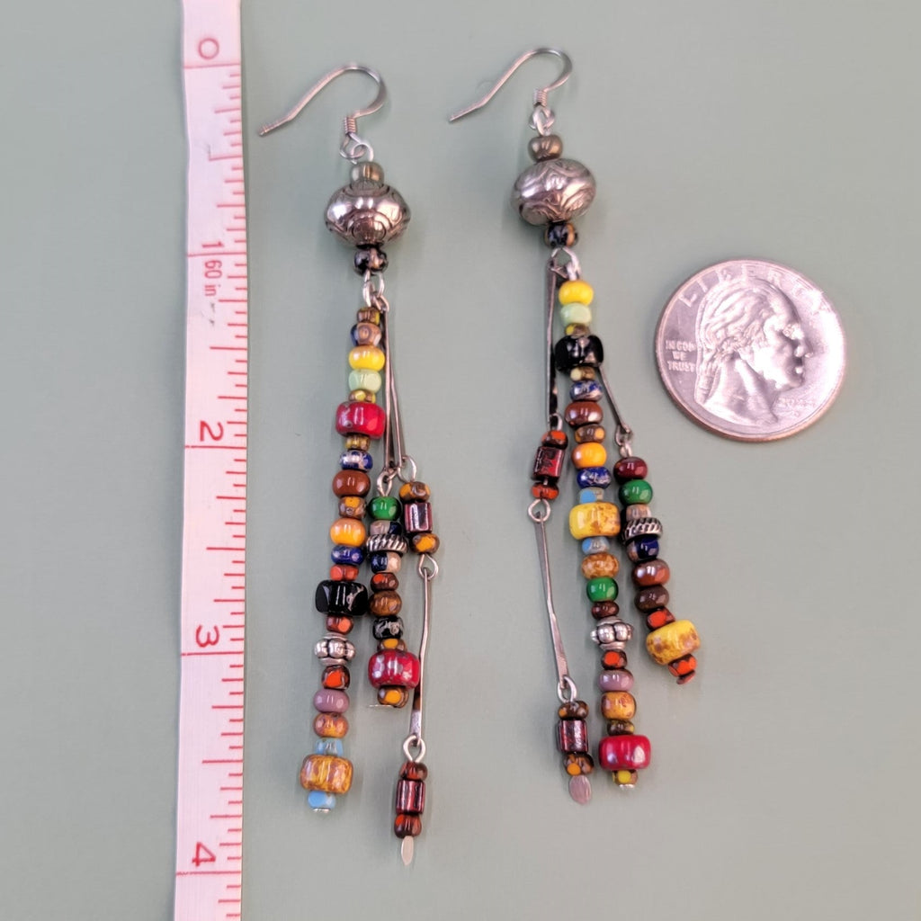 Long, dangly, colorful Boho earrings featuring three drops filled with richly-colored Picasso glass beads and silver-colored accents. 