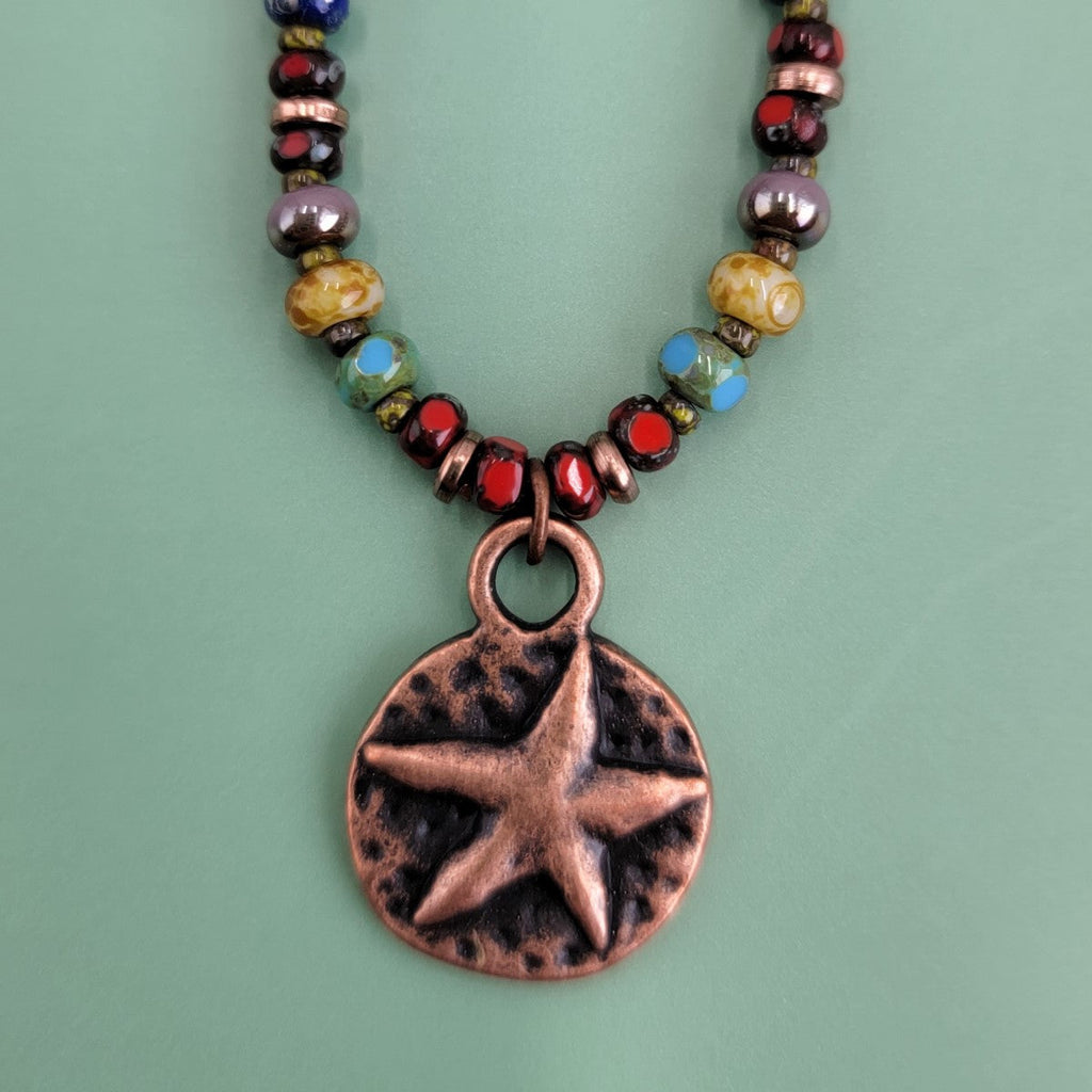 Handmade Boho necklace featuring a rustic antiqued copper sea star and an array of bright Picasso glass beads in multiple colors. Coastal-inspired artisan jewelry for a touch of seaside elegance.