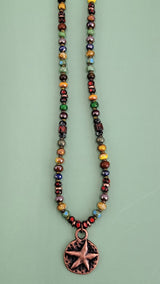 Handmade Boho necklace featuring a rustic antiqued copper sea star and an array of bright Picasso glass beads in multiple colors. Coastal-inspired artisan jewelry for a touch of seaside elegance.
