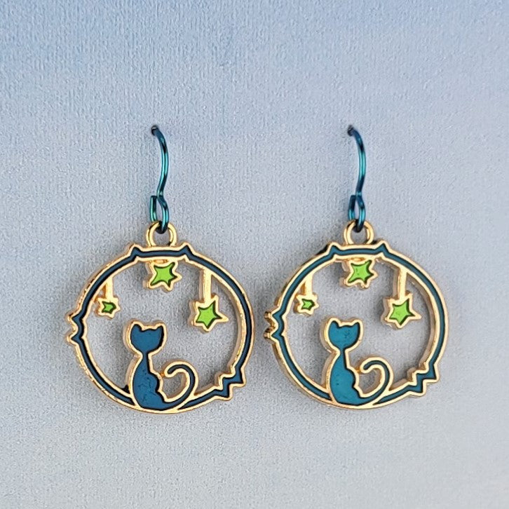 Handmade cat and star earrings including blue enamel cat on blue background looking at green enamel stars