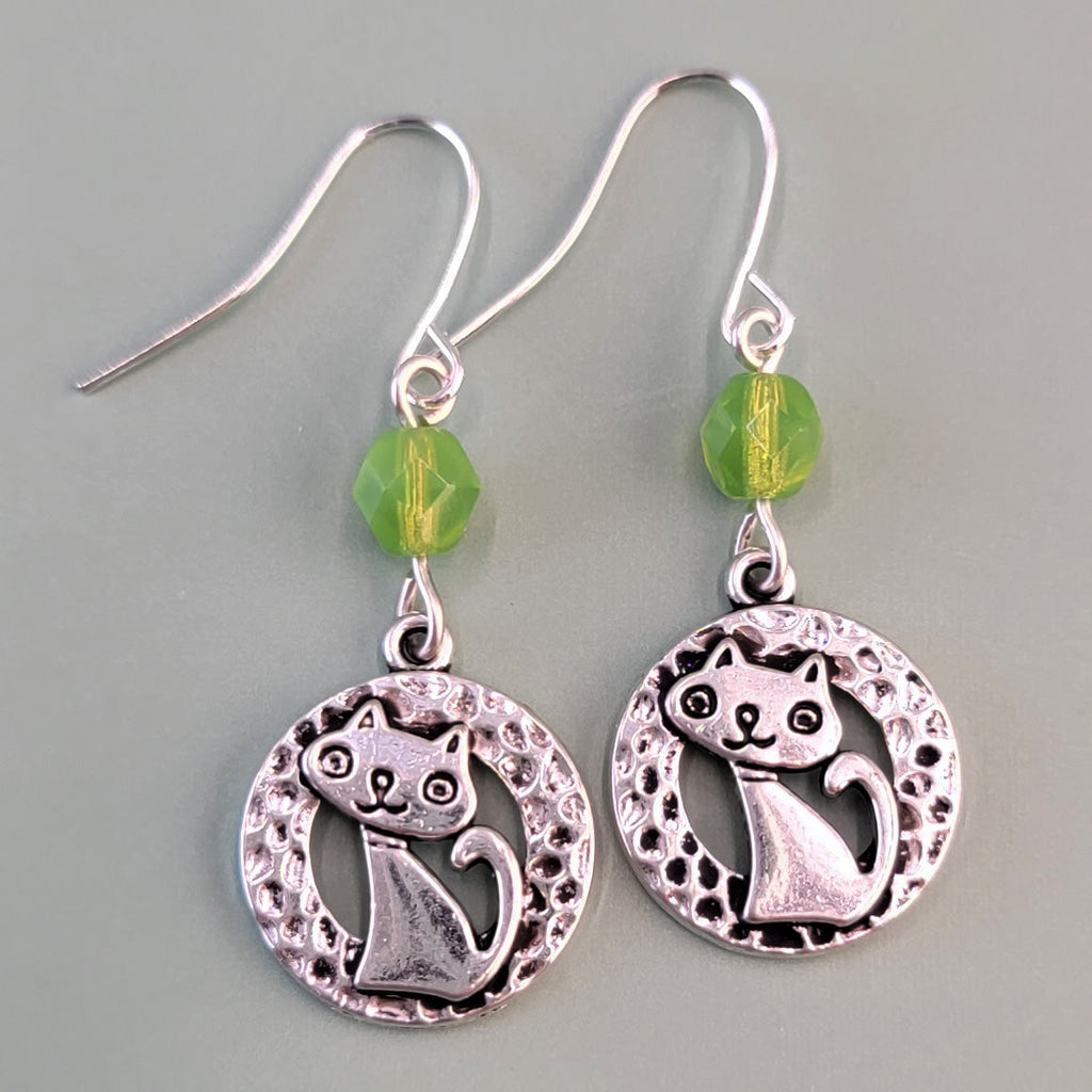 Hypoallergenic silver cat earrings have hammered silver rings with sweet smiling kittens and green Czech glass accent beads
