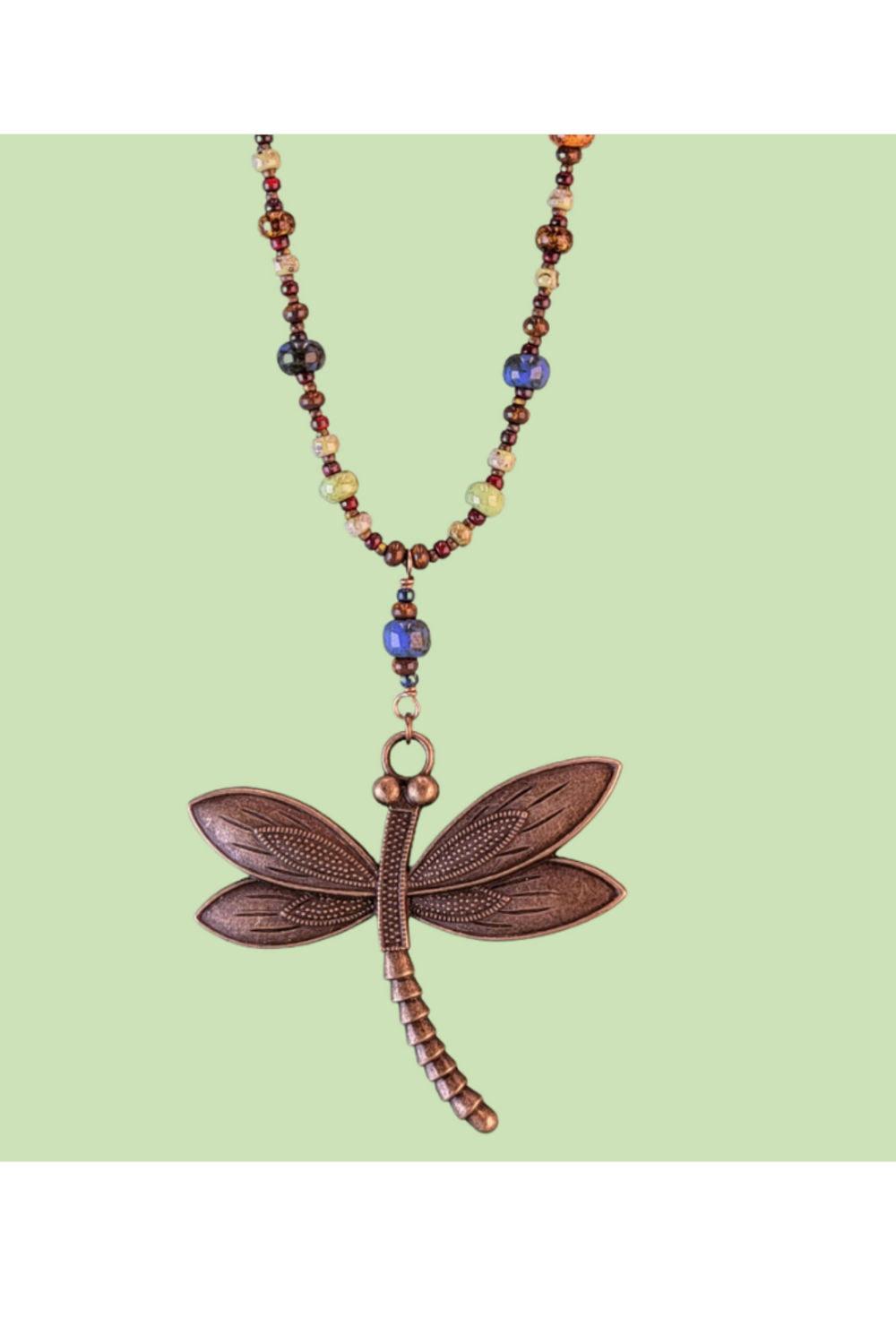 Close-up of an intricate 2.5-inch antiqued bronze dragonfly pendant showing detailed wing textures and earthy Picasso glass bead accents.